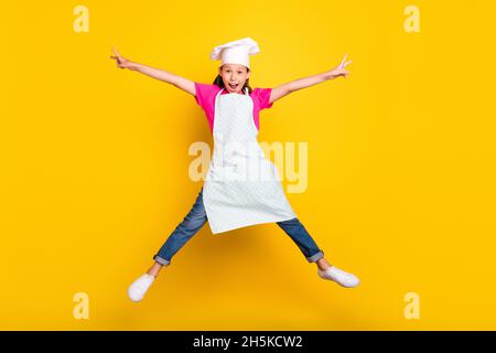 Photo de l'énergie insouciante petite fille saut lever les mains étoile forme porter tablier chapeau chaussures isolé couleur jaune fond Banque D'Images