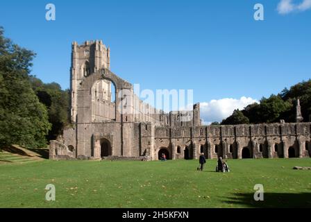Personnes marchant sur l'herbe en face de la Nave et du Grand Cloître des Fontaines Abbey, Aldfield, près de Ripon, North Yorkshire, Angleterre Banque D'Images