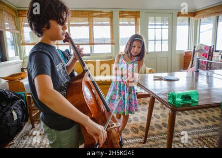 Un garçon donne un concert de violoncelle à une petite souris dans une boîte tandis que la sœur regarde Banque D'Images