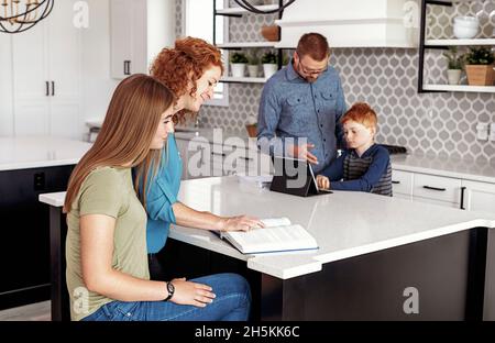 Les parents qui aident le jeune fils et la fille adolescente à faire leurs devoirs dans la cuisine; Edmonton, Alberta, Canada Banque D'Images