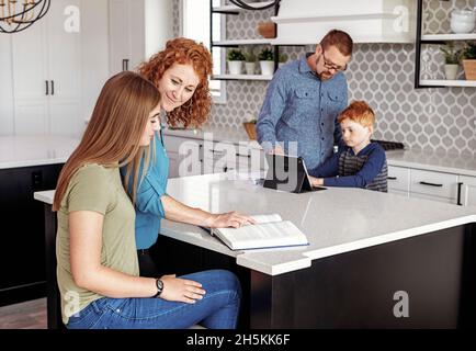 Les parents qui aident le jeune fils et la fille adolescente à faire leurs devoirs dans la cuisine; Edmonton, Alberta, Canada Banque D'Images