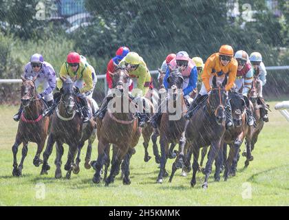 Des chevaux de course en action sont criblés par des jockeys, se sont rassemblés, se faisant courir à l'hippodrome de Worcester sous la pluie d'été, au Royaume-Uni. Banque D'Images