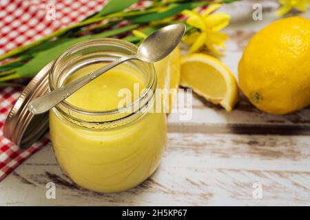 Un bocal avec du citron curd fait maison à côté de quelques citrons sur une vieille table en bois.Vue en hauteur. Banque D'Images