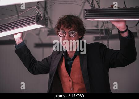 Homme dans des vêtements et des lunettes à la mode posé près du mur de briques Banque D'Images