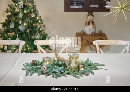 table pour le dîner de noël avec boule verte avec renne doré et bougies. arbre de noël décoré, étoile dorée et figurine de bonhomme de neige dans le b Banque D'Images