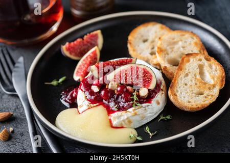 Fromage camembert cuit avec sauce aux canneberges, figues et pain grillé sur l'assiette, servi avec un verre de vin rouge.Hors-d'œuvre gastronomique Banque D'Images