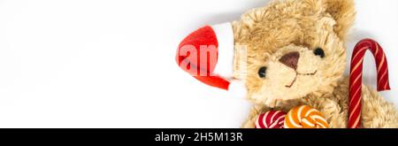 Bunner avec un ours en peluche Teddy dans un chapeau rouge du Père Noël sur une oreille, tenant la canne à sucre et deux sucettes rayées dans ses pattes.Fond blanc, CO Banque D'Images