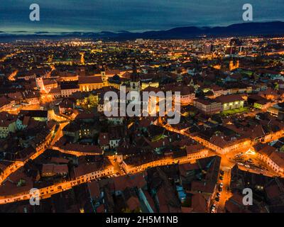 Photographie aérienne du centre-ville de Sibiu prise d'un drone au coucher du soleil avec lumières de la ville allumées.Vue depuis le dessus de Sibiu, Roumanie. Banque D'Images