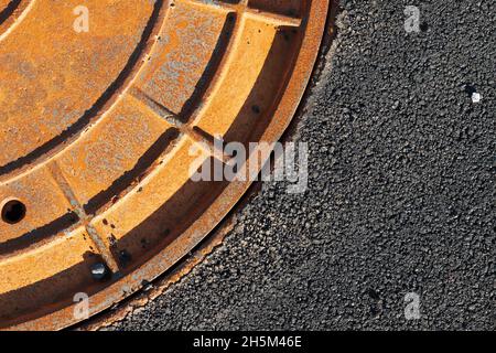 Trou d'égout rouge rouillé dans une route tarmac, fragment abstrait de gros plan Banque D'Images