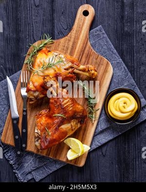 tiges de porc grillées croustillantes sur une planche de bois avec romarin, quartiers de citron et moutarde, vue verticale depuis le dessus Banque D'Images