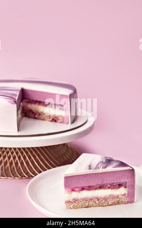 Délicieux gâteau de mousse de litchi et de framboise sur un support et trancher avec les couches et la texture affichées sur fond lilas.Menu du restaurant et concept de confiserie.Gros plan.Copier l'espace. Banque D'Images