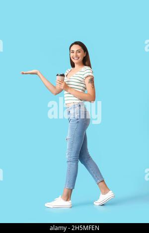 Belle femme avec une tasse de café montrant quelque chose sur fond de couleur Banque D'Images