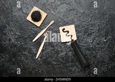 Poudre de dent de charbon actif, tube de dentifrice et brosses à dents en bambou sur fond sombre Banque D'Images