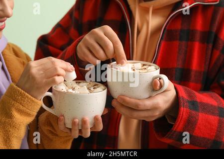 Jeune couple en vêtements d'hiver et avec des tasses de chocolat chaud sur fond clair, gros plan Banque D'Images