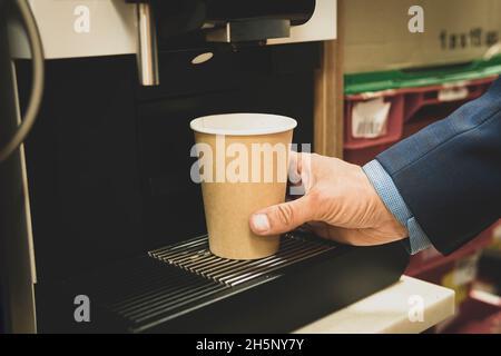 l'homme prend le café d'un distributeur automatique. vue courte de l'homme d'affaires en appuyant sur le bouton de la cafetière tout en préparant le café à emporter. Banque D'Images