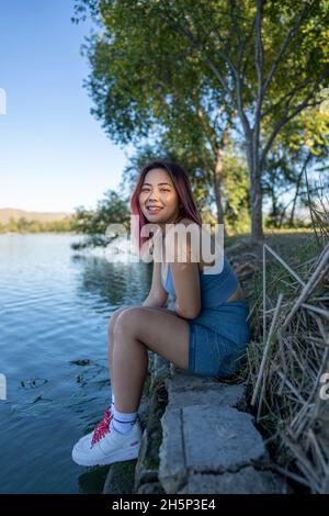 Jeune femme asiatique à Dappled lumière du soleil assis sur la rive d'un lac idyllique Banque D'Images