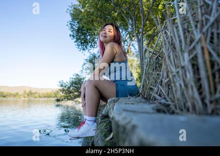 Jeune femme asiatique à Dappled lumière du soleil assis sur la rive d'un lac idyllique Banque D'Images