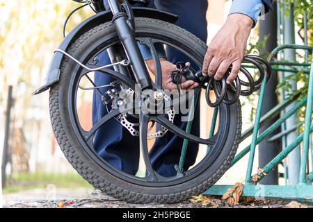 main tenant la clé pour déverrouiller le vélo.Un employé en costume ou un homme d'affaires enchaîne son vélo électrique près du travail. Banque D'Images