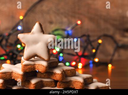 Des étoiles de cannelle empilées sur une table en bois avec des lumières de Noël colorées Banque D'Images
