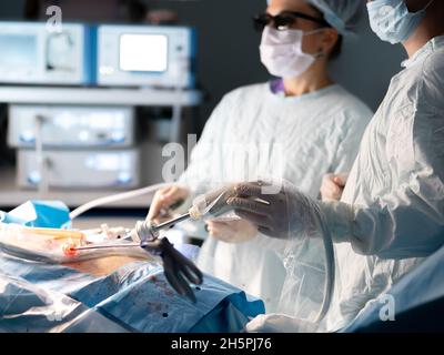 Concentration sélective sur la main du chirurgien avec une pince laparoscopique avec un trocart.Une femme chirurgien portant des lunettes 3D effectue une chirurgie de haute technologie peu invasive sur un arrière-plan flou. Banque D'Images