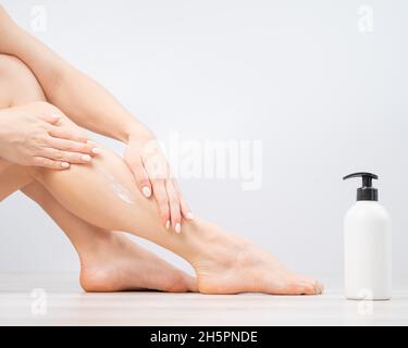 Femme applique un hydratant sur ses jambes sur un fond blanc. La fille prend soin de la peau et utilise la crème. Banque D'Images