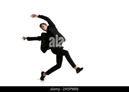 Le jeune homme en costume d'affaires noir se déplace isolé sur fond blanc.Art, mouvement, action, flexibilité, inspiration concept. Banque D'Images