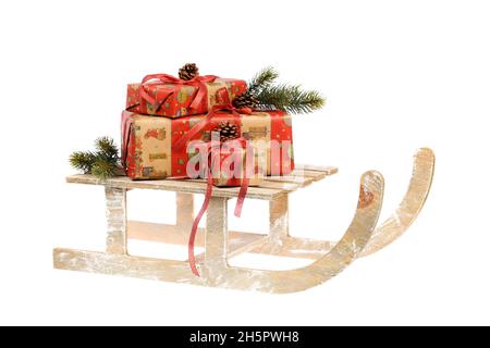 Pile de cadeaux enveloppés de Noël avec noeud rouge, brindilles de pin et cônes de pin sur un traîneau en bois vintage, isolé sur blanc.Concept de shopping de Noël Banque D'Images