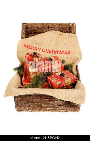 Cadeaux de Noël emballés avec rubans rouges sur un sac de jute avec texte « Joyeux Noël », décoré avec des cônes de pin et des brindilles de pin dans un panier en osier, isol Banque D'Images