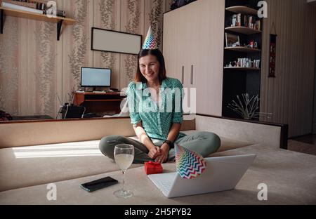 femme célébrant son anniversaire en ligne en période de quarantaine par le biais d'un appel vidéo de la fête virtuelle.Éclosion de coronavirus 2020.Femme ouvrant un cadeau et ont des émotions positives. Banque D'Images