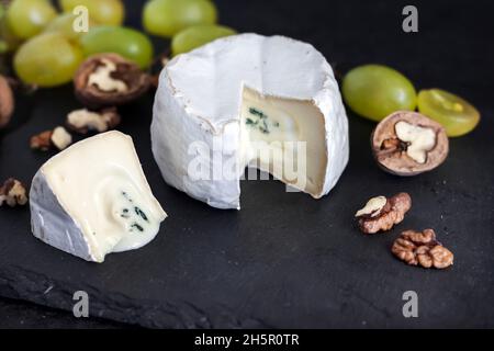 Type Brie de fromage.Fromage doux avec raisins et noix sur fond noir Banque D'Images