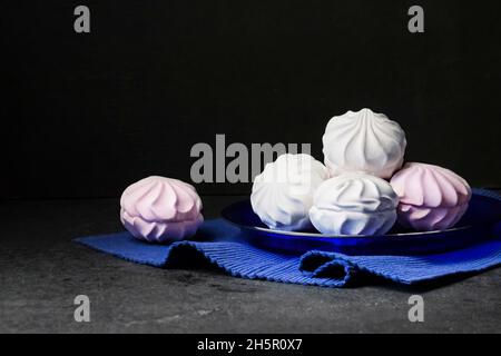 Guimauve blanche et rose sur plaque bleue sur fond noir. Banque D'Images