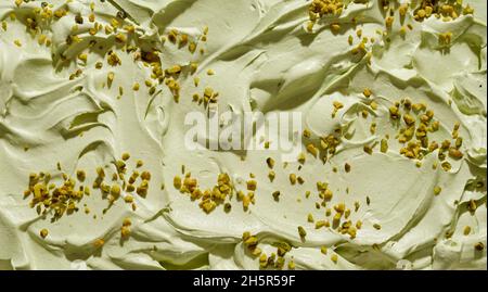 Crème glacée crémeuse à la pistache avec des noix fraîches hachées dans une texture de fond plein cadre avec gros plan sur la surface avec des tourbillons et des crêtes Banque D'Images