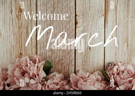 Bienvenue texte typographique de mars avec bouquet de fleurs roses sur fond de bois Banque D'Images