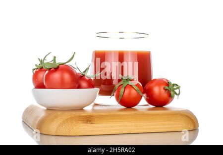 Une tasse de verre avec jus de tomate et plusieurs tomates sur un plateau en bambou, gros plan, isolé sur blanc. Banque D'Images