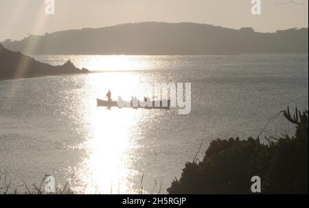 Tresco dames équipe de gig d'aviron, oars reposant, sur l'eau argentée au coucher du soleil.Tourné dans le canal de la mer entre Tresco et Bryher dans les îles de Scilly. Banque D'Images