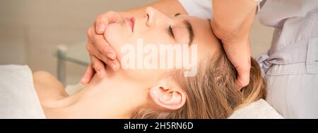 Les mains du cosmétologue font un massage facial sur le front et le menton de la jeune femme au spa Banque D'Images