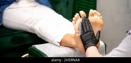 Hydrater les pieds.Mains de maître de pédicure en gants noirs entretien des pieds féminins.Massage des pieds.Concept de salon de beauté pédicure Banque D'Images