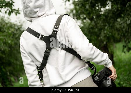 Déchargement d'une sangle de caméra sur une femme dans une veste blanche sur la nature dans le parc, forêt. Banque D'Images