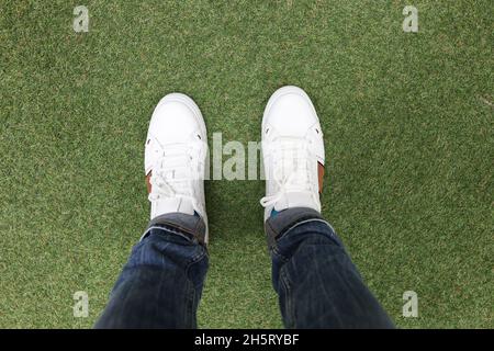 Pieds de sexe masculin dans des baskets blanches debout sur une pelouse en gros plan Banque D'Images