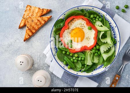 Poivrons rouges farcis avec des œufs, des feuilles d'épinards, des pois verts et des microverts sur une assiette de petit déjeuner sur fond de table gris clair. Vue de dessus. Banque D'Images