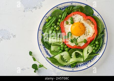 Poivrons rouges farcis avec des œufs, des feuilles d'épinards, des pois verts et des microverts sur une assiette de petit déjeuner sur fond de table gris clair. Vue de dessus. Banque D'Images