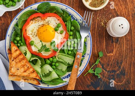 Poivrons rouges farcis avec des œufs, des feuilles d'épinards, des pois verts et des microverts sur une assiette de petit déjeuner sur fond de table en bois. Vue de dessus. Banque D'Images