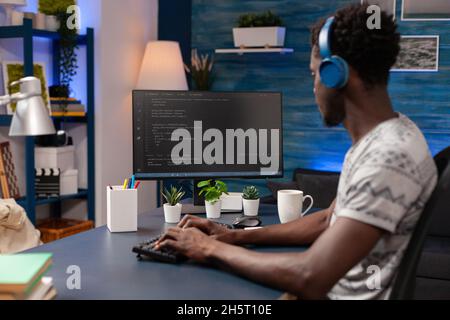 Un coder américain africain programmant un code d'entreprise à l'aide d'un système de sécurité réseau fonctionnant à distance de chez lui.Programmeur homme naviguant sur le serveur d'entreprise de l'ordinateur.Logiciel de sécurité Banque D'Images