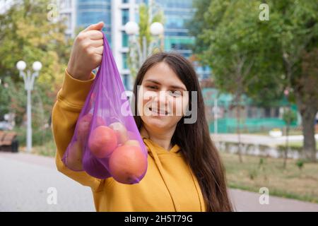 La femme montre un sac en tissu violet transparent avec des fruits. Banque D'Images