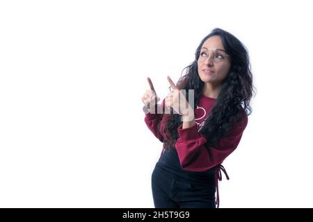 Jolie femme hispanique latine avec de longs cheveux épais portant des lunettes sur fond blanc à l'intérieur faisant des expressions et des gestes, pointant avec les deux mains, Banque D'Images