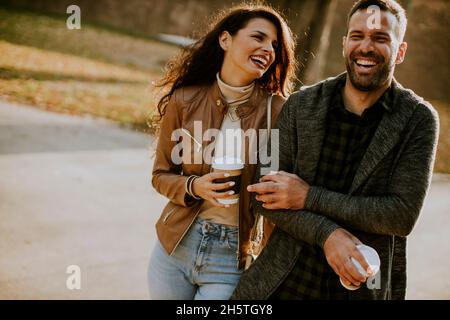 Beau jeune couple marchant dans le parc d'automne avec le café pour aller tasses dans les mains Banque D'Images