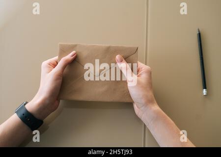 Gros plan vue en grand angle d'une jeune femme méconnue tenant dans une enveloppe de mains avec une lettre reçue assise à une table. Banque D'Images