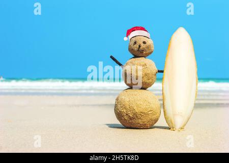 Sandman joyeuse surfer avec une planche de surf sur le sable contre l'eau de mer turquoise. Noël et nouvel an concept sur une plage tropicale. Des couleurs vives. concept o Banque D'Images