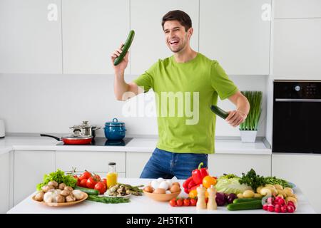 Portrait de sympathique gars gai dansant avec le concombre préparant le repas dans la cuisine blanche claire maison à l'intérieur Banque D'Images