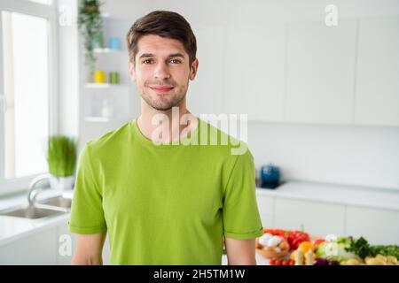 Photo portrait brunette homme en chemise verte souriant debout sur la cuisine à la maison Banque D'Images